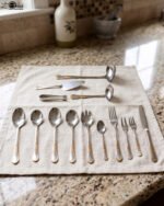72-piece stainless steel cutlery set with gold-embossed handles arranged on a neutral linen cloth