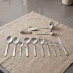 72-piece silver stainless steel cutlery set with embossed gold handles displayed on a linen mat.