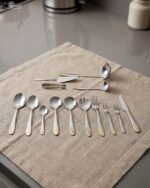 72-piece silver stainless steel cutlery set with embossed gold handles displayed on a linen mat.