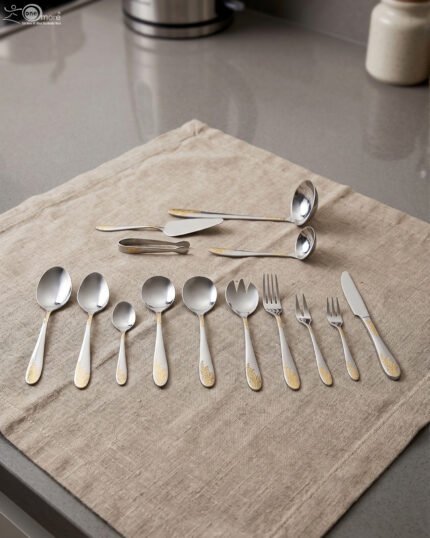 72-piece silver stainless steel cutlery set with embossed gold handles displayed on a linen mat.