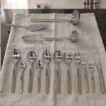 72-piece stainless steel cutlery and serving set with dual-tone gold textured handles laid out on a linen cloth.