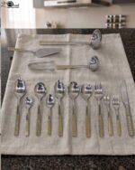 72-piece stainless steel cutlery and serving set with dual-tone gold textured handles laid out on a linen cloth.
