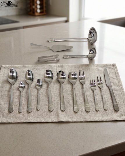 A Diverse Arrangement of Polished Silver-Toned Cutlery on a Textured Linen Mat, Featuring 12-Person Service and Loose Ladles, a Cake Server, and Tongs in the Background.