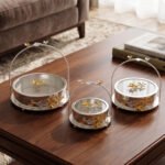 3-piece luxury silver decorative serving dishes with gold floral accents and metallic handles displayed on a wooden coffee table.