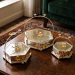 Three hexagonal silver and gold floral decorative serving dishes with handles resting on a wooden coffee table