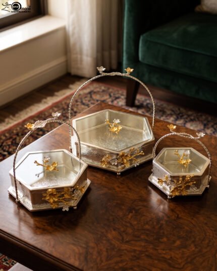 Three hexagonal silver and gold floral decorative serving dishes with handles resting on a wooden coffee table