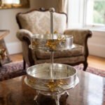 Two-tiered textured silver serving stand with gold floral accents displayed on a wooden table.
