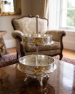 Two-tiered textured silver serving stand with gold floral accents displayed on a wooden table.