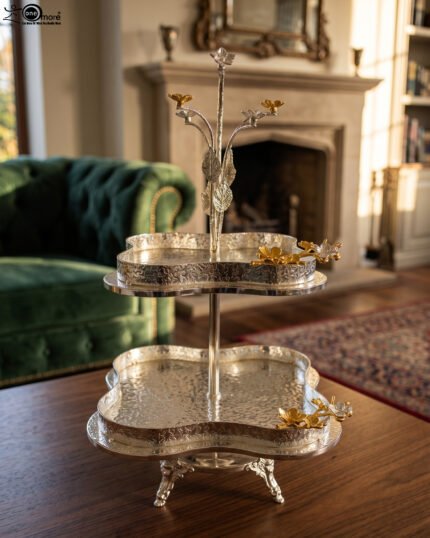 Two-tier silver hammered decorative serving tray with gold floral accents resting on a wooden coffee table in an elegant living room setting.