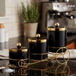 Luxury 3-piece black and gold ceramic storage jar set with golden lids arranged on an elegant gold metal cart stand on a modern kitchen countertop.
