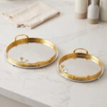 Round hammered metal decorative serving tray with dual gold handles and detailed silver and gold floral branch accent on a kitchen countertop.