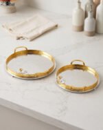 Round hammered metal decorative serving tray with dual gold handles and detailed silver and gold floral branch accent on a kitchen countertop.