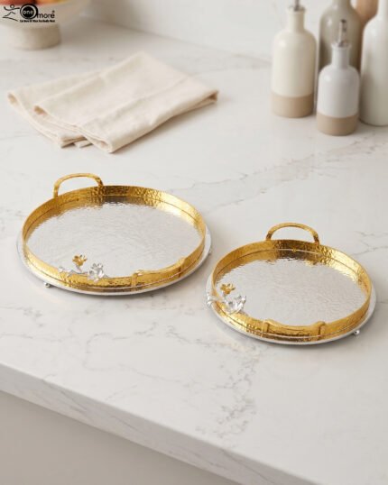 Round hammered metal decorative serving tray with dual gold handles and detailed silver and gold floral branch accent on a kitchen countertop.