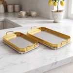 Set of two luxury gold and silver rectangular decorative serving trays with Greek key pattern borders resting on a white marble countertop.