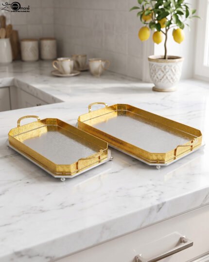 Set of two luxury gold and silver rectangular decorative serving trays with Greek key pattern borders resting on a white marble countertop.