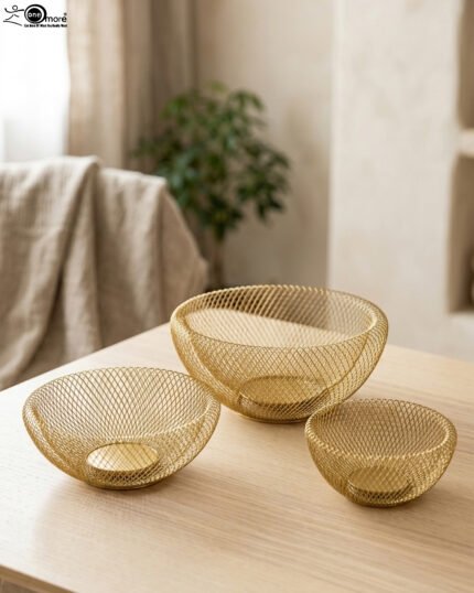 Set of three gold mesh decorative wire bowls sitting on a light wooden table in a brightly lit modern living room setup.