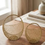 Set of two gold woven wire metal decorative baskets with coiled handles displayed on a wooden table