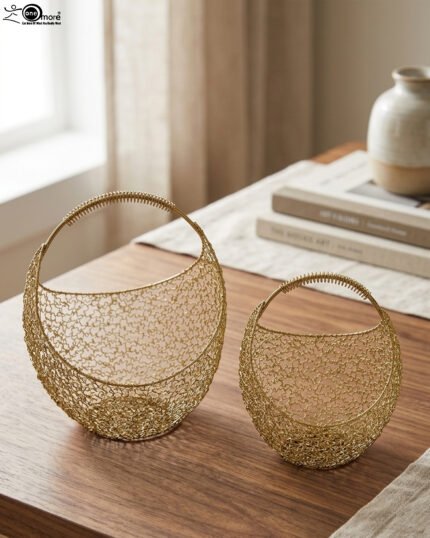 Set of two gold woven wire metal decorative baskets with coiled handles displayed on a wooden table