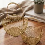 Two gold mesh metal decorative baskets with coiled top handles on a wooden table.
