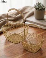 Two gold mesh metal decorative baskets with coiled top handles on a wooden table.