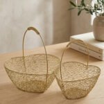Two heart-shaped decorative gold wire mesh baskets with single handles set on a wooden table.