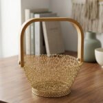 Gold woven wire decorative basket with a natural wooden handle sitting on a wooden tabletop