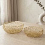 Set of two round gold woven wire decorative metal baskets sitting on a light wooden tabletop.
