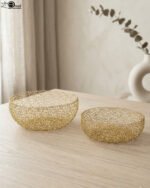 Set of two round gold woven wire decorative metal baskets sitting on a light wooden tabletop.