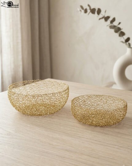 Set of two round gold woven wire decorative metal baskets sitting on a light wooden tabletop.