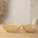 Two gold woven wire decorative metal baskets sitting on a light wooden tabletop.