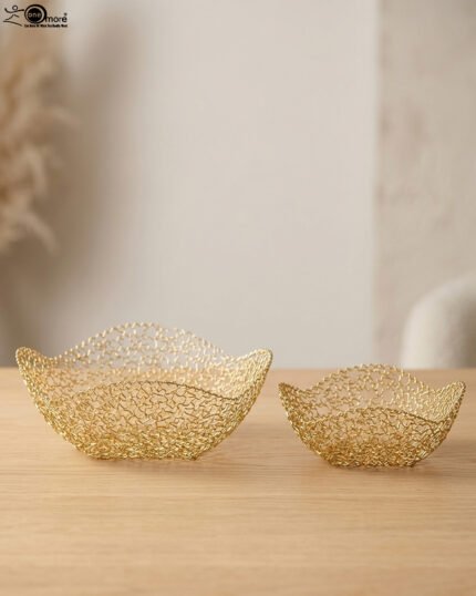 Two gold woven wire decorative metal baskets sitting on a light wooden tabletop.