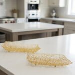 Pair of decorative gold wire mesh baskets with footed base displayed on a white kitchen countertop