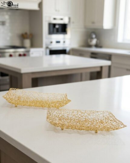 Pair of decorative gold wire mesh baskets with footed base displayed on a white kitchen countertop