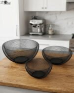Set of three round black wire mesh decorative metal baskets displayed on a wooden kitchen countertop.