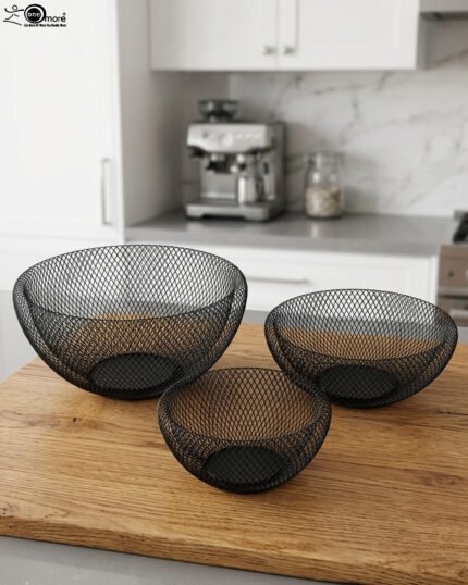 Set of three round black wire mesh decorative metal baskets displayed on a wooden kitchen countertop.