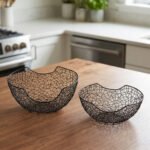 Set of two modern black wire mesh decorative baskets sitting on a wooden kitchen island countertop.