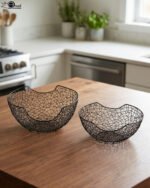 Set of two modern black wire mesh decorative baskets sitting on a wooden kitchen island countertop.