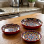 Three vibrant ceramic decorative Moroccan plates featuring intricate mandala patterns in red, blue, and yellow arranged on a wooden countertop.
