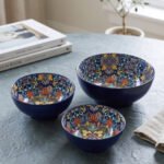 Set of three hand-painted decorative Marrakech ceramic bowls with colorful bohemian patterns and navy blue exteriors on a slate table.
