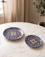 Two vibrant blue, yellow, and red decorative Marrakech ceramic plates displaying intricate mosaic patterns on a white marble surface in 8-inch and 10-inch sizes.