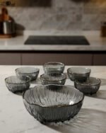 7-piece grey ribbed glass fruit set featuring one large serving bowl and six small bowls with elegant gold rims, displayed on a kitchen counter.