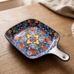 Square 6.5-inch Marrakech ceramic serving dish with colorful mosaic mandala patterns and an integrated handle on a wooden table.