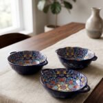 Three hand-painted decorative Marrakech ceramic bowls with intricate bohemian patterns and handles arranged on a dining table runner.