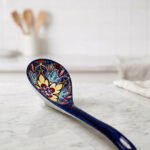 Handcrafted decorative Marrakech ceramic spoon with vibrant blue, yellow, and red bohemian floral patterns resting on a marble countertop