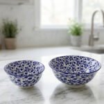 Pair of decorative blue and white Marrakesh ceramic floral bowls in 6-inch and 8-inch sizes sitting on a marble kitchen countertop.
