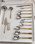 72-piece stainless steel cutlery set with gold trim handles and specialty serving utensils displayed on a white tray.