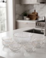 7-piece grey ribbed glass fruit set featuring one large serving bowl and six small bowls with elegant gold rims, displayed on a kitchen counter.