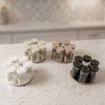 Modern rotating spice rack organizer set with 6 clear glass jars and gold-accented lids on a granite kitchen countertop.