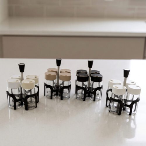 Four-piece clear glass spice jar set with lid options sitting in a black metal holder on a kitchen countertop.