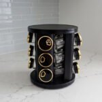 Modern 12-piece rotating black and gold spice rack organizer with glass jars on a white marble kitchen countertop